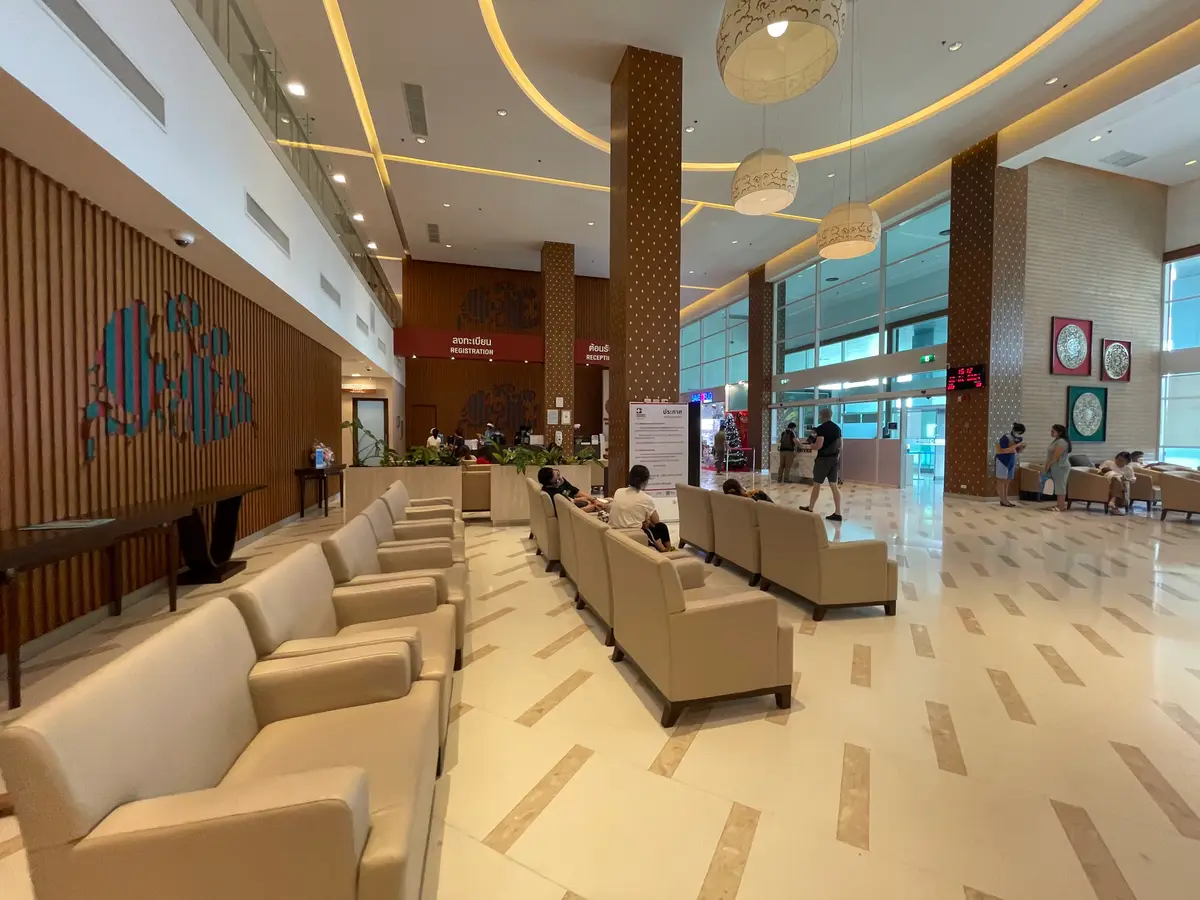 Wide hospital lobby with beige sofas along a wood-panelled wall under a high ceiling.