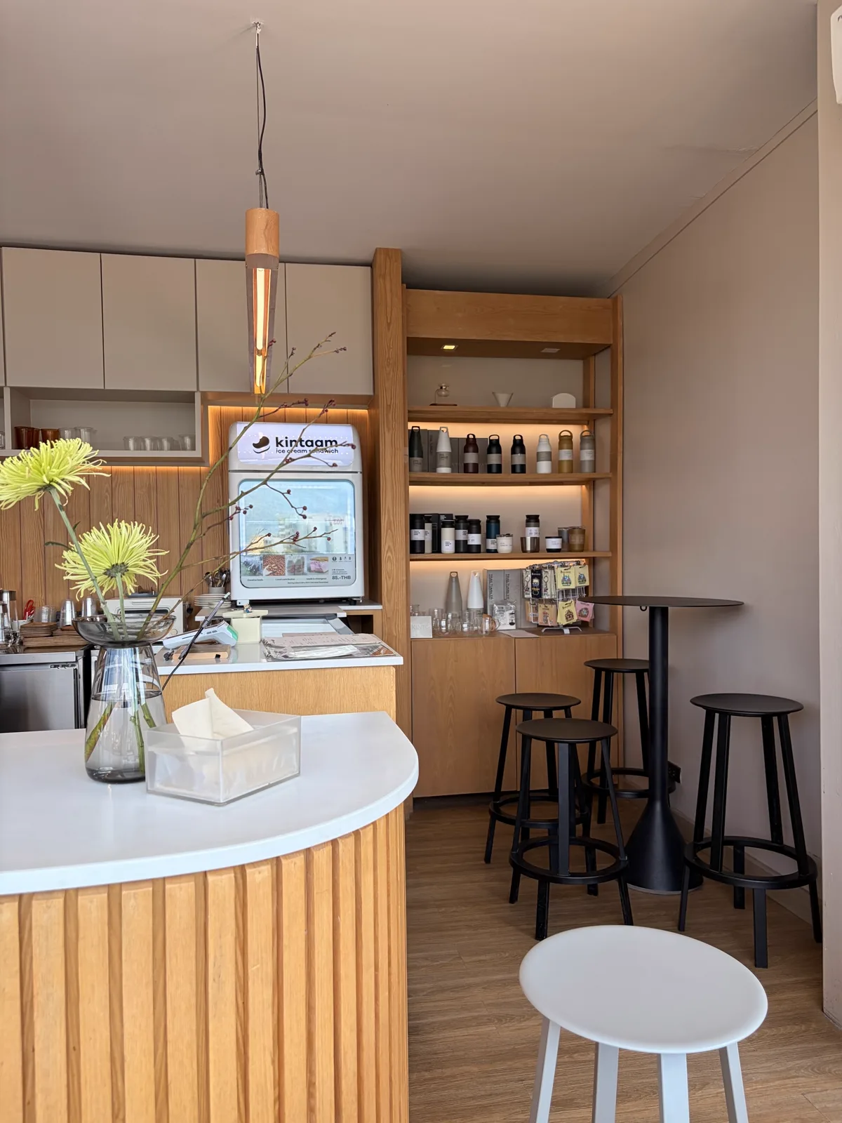 Counter area with an ice cream machine, wooden shelves and black stools