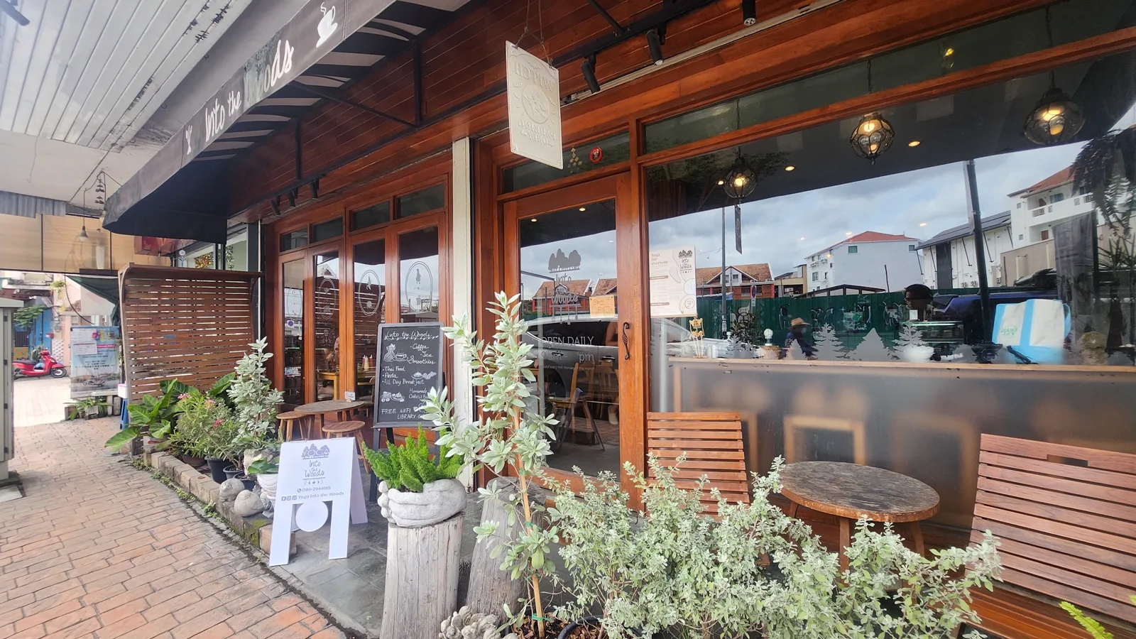 Wooden storefront with an Into the Woods awning, sign boards and potted plants on the sidewalk