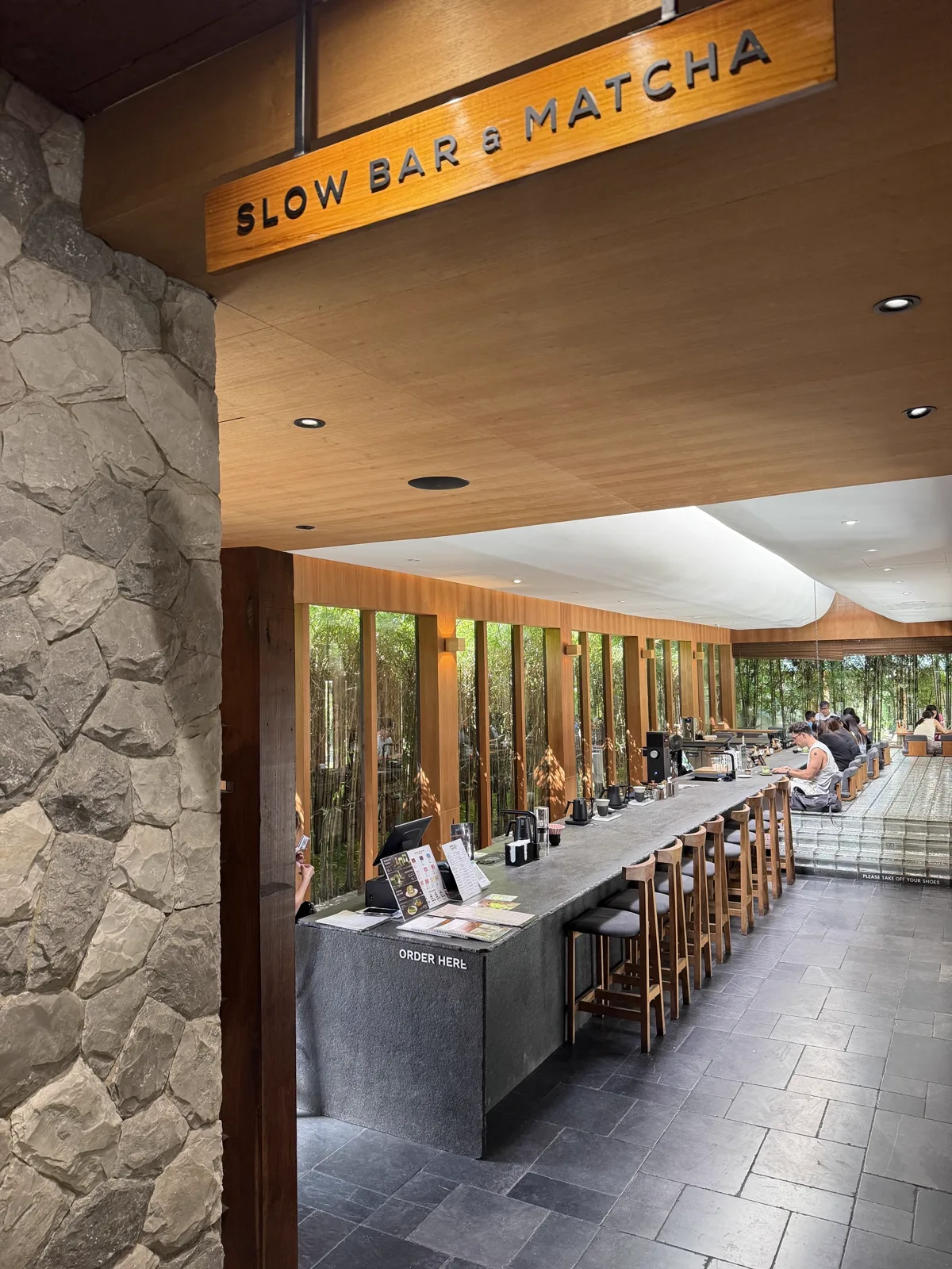 Order bar under a wooden sign reading Slow Bar and Matcha, beside a stone pillar and bamboo wall
