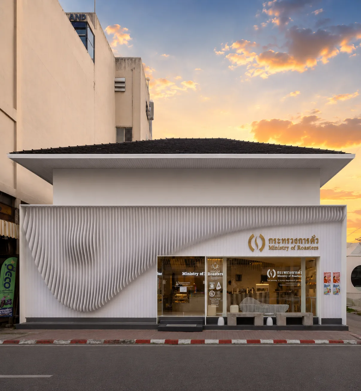 Street facade with white walls, dark tiled roof, curved wave-patterned panel and a gold Ministry of Roasters sign