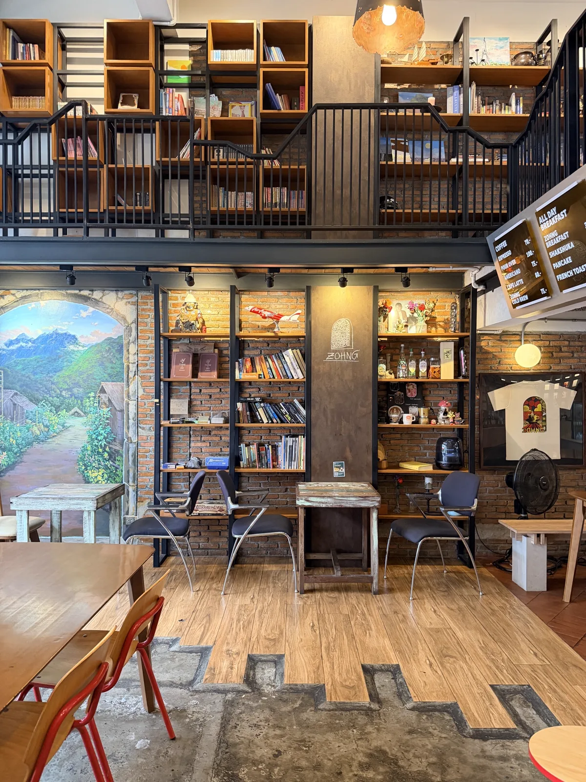 Brick-walled room with bookshelves, a chalk ZOHNG sign and empty wooden tables