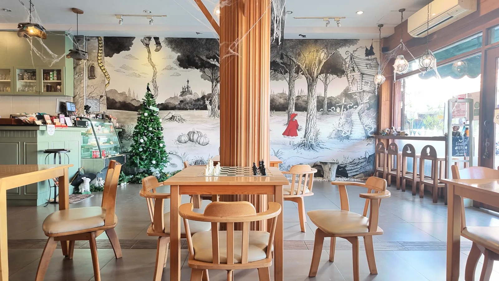 Wide room with a black and white forest mural, a Christmas tree and a chessboard table