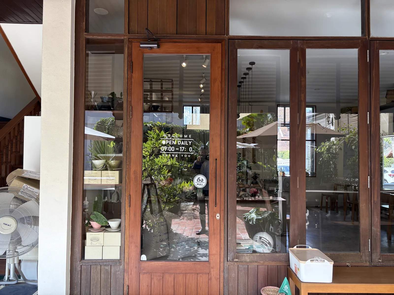 Wooden glass entrance door with an opening hours sticker and plants inside