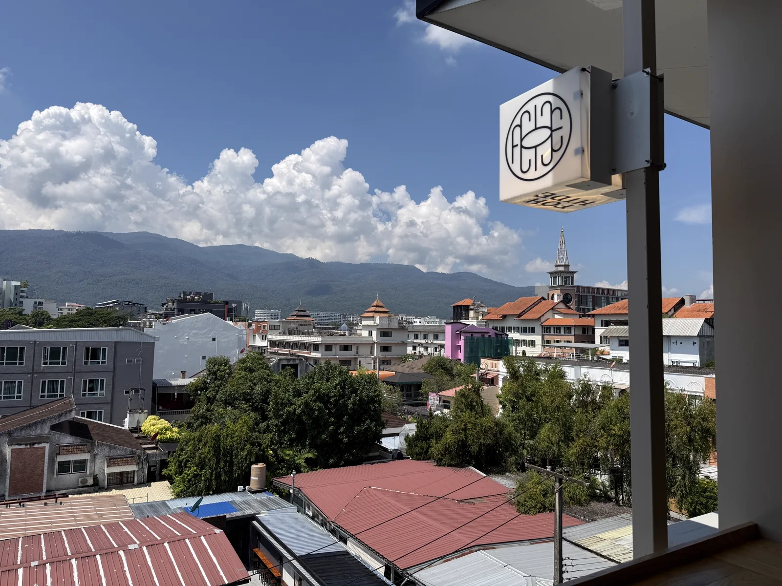 Rooftop view past a FOHHIDE sign over red roofs, a clock tower and mountains