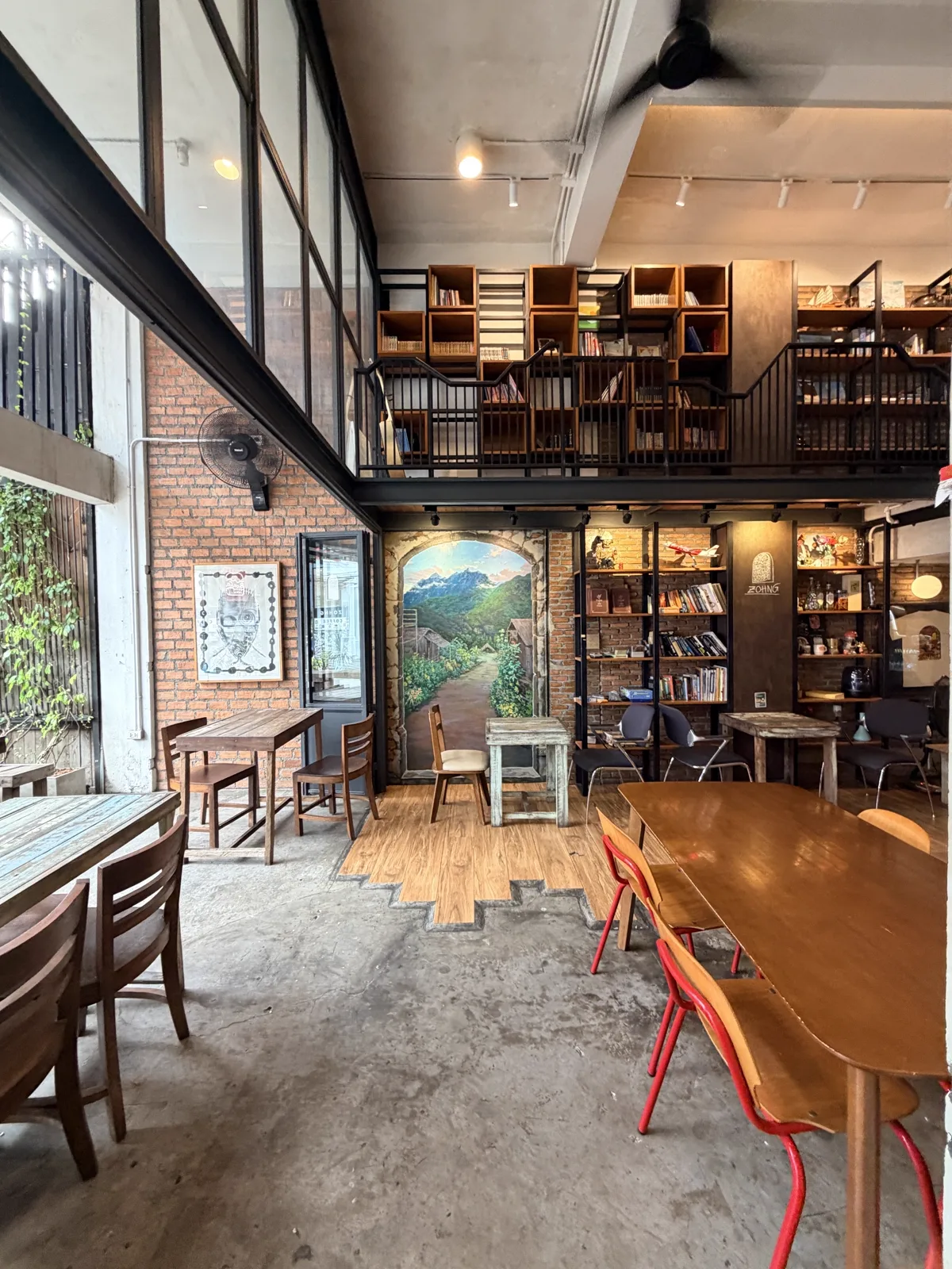 Wide room with a mountain village mural, bookshelves, a mezzanine and red chairs
