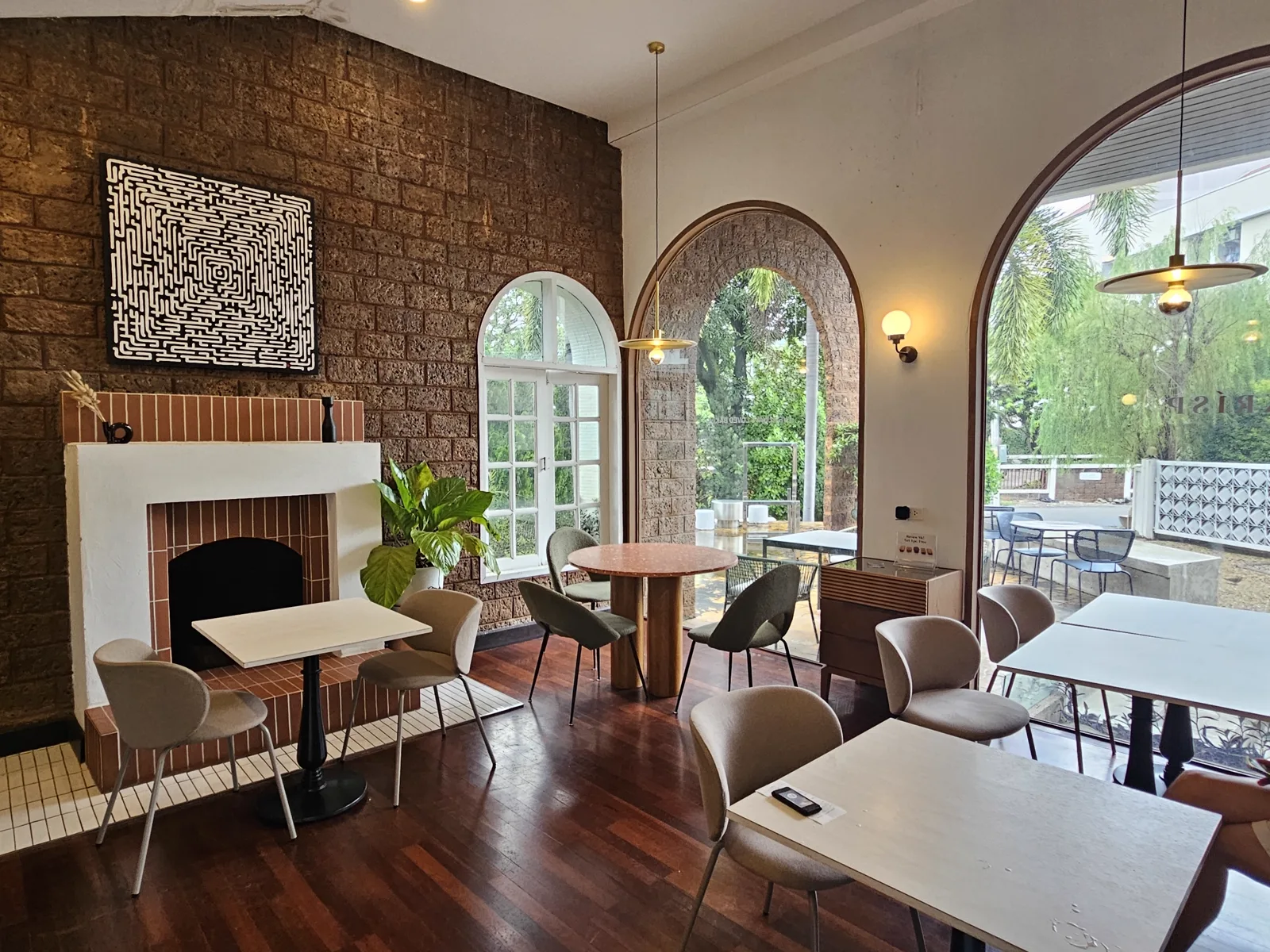Dining room with a brick feature wall, fireplace, arched windows and empty wooden tables