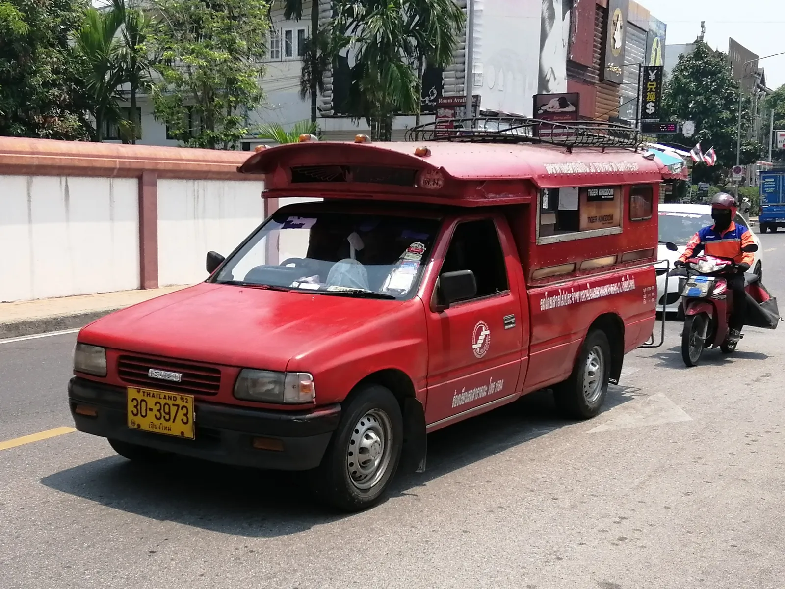 Red pickup truck with a covered passenger bed driving along a city street