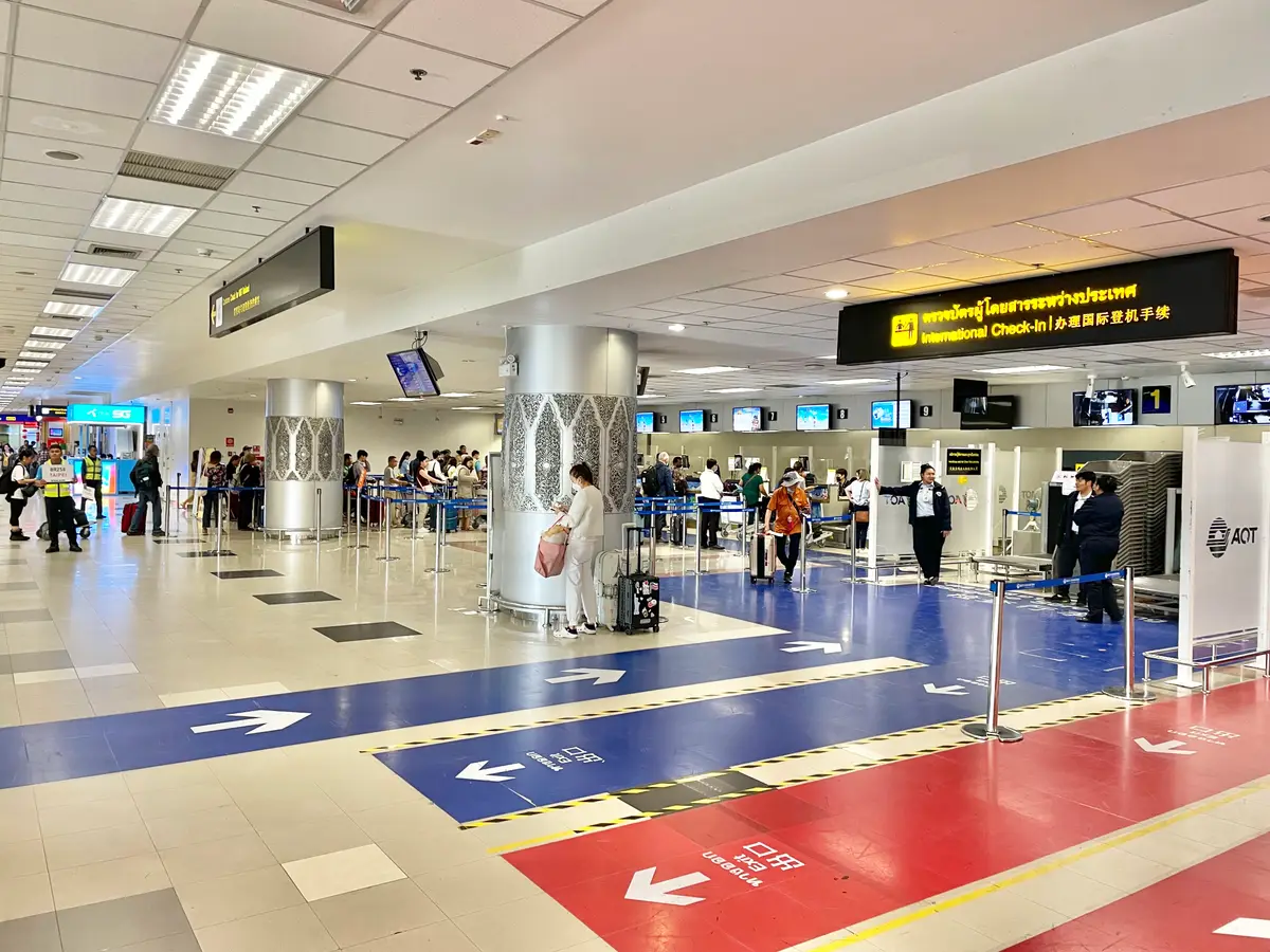 Bright terminal hall with coloured floor arrows and passengers queuing under an international check-in sign.