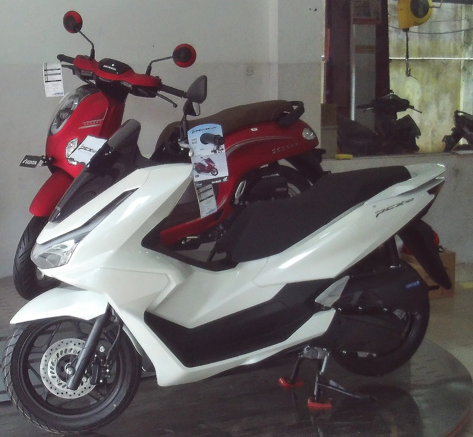 White Honda scooter with a red scooter behind it on a dealer's floor.