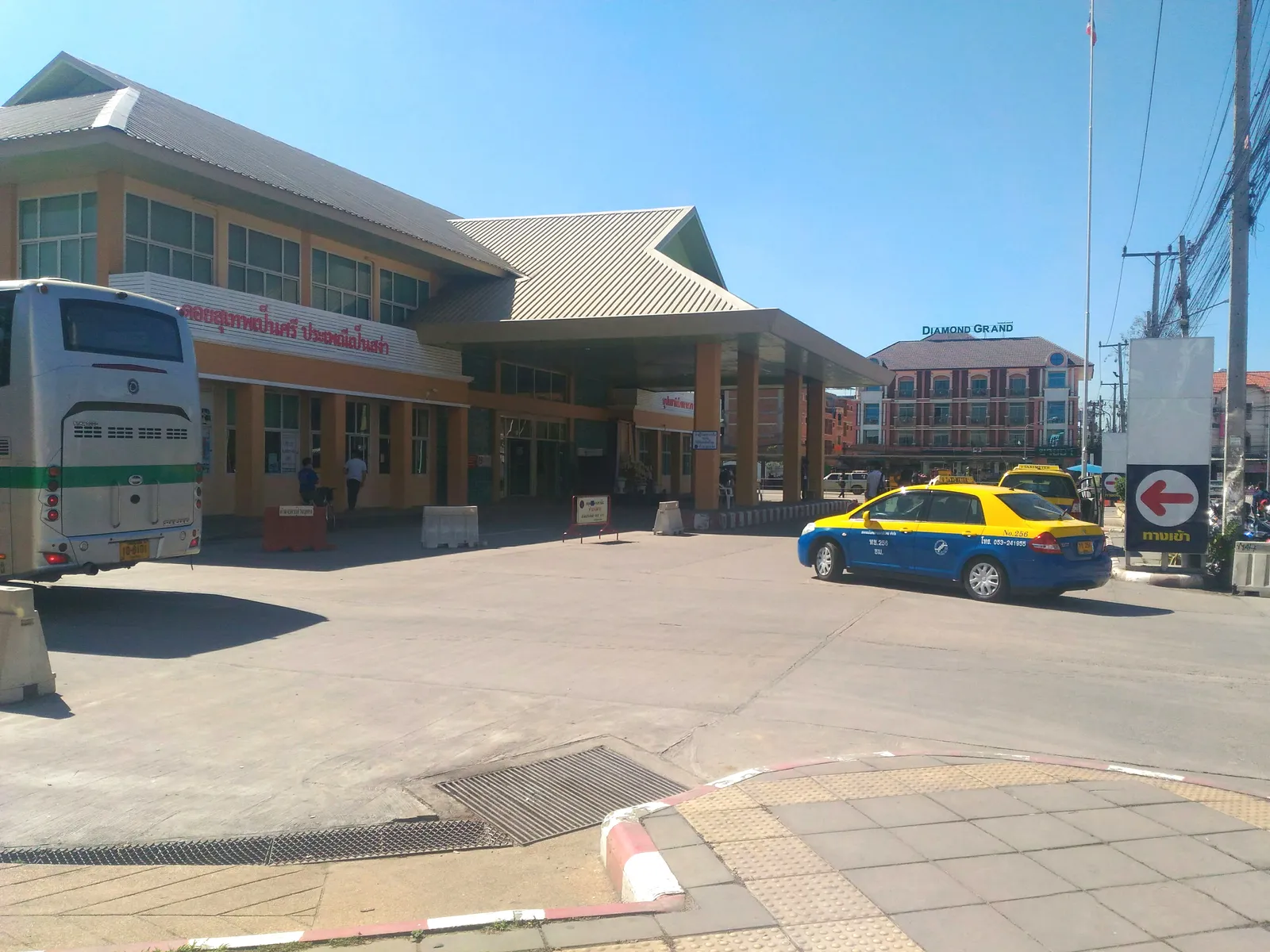 Terminal building with an orange and grey roof, a bus on the left and a blue and yellow taxi in front of the entrance canopy.