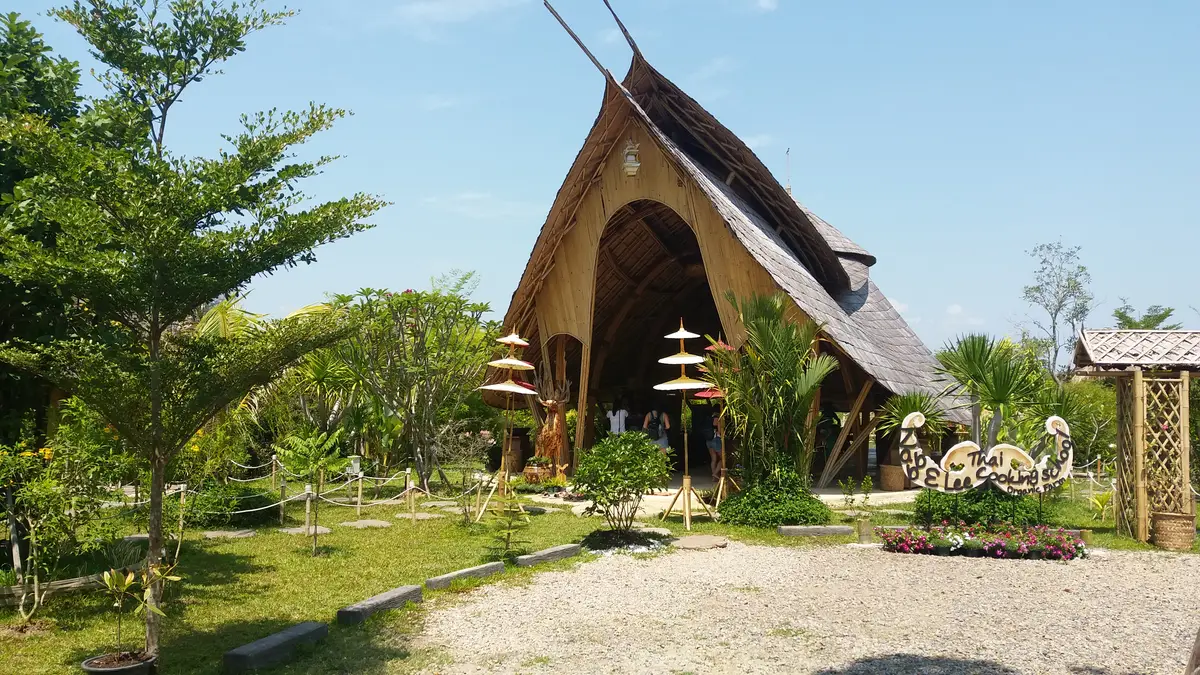 A curved bamboo and thatch building behind a garden and a gravel path.