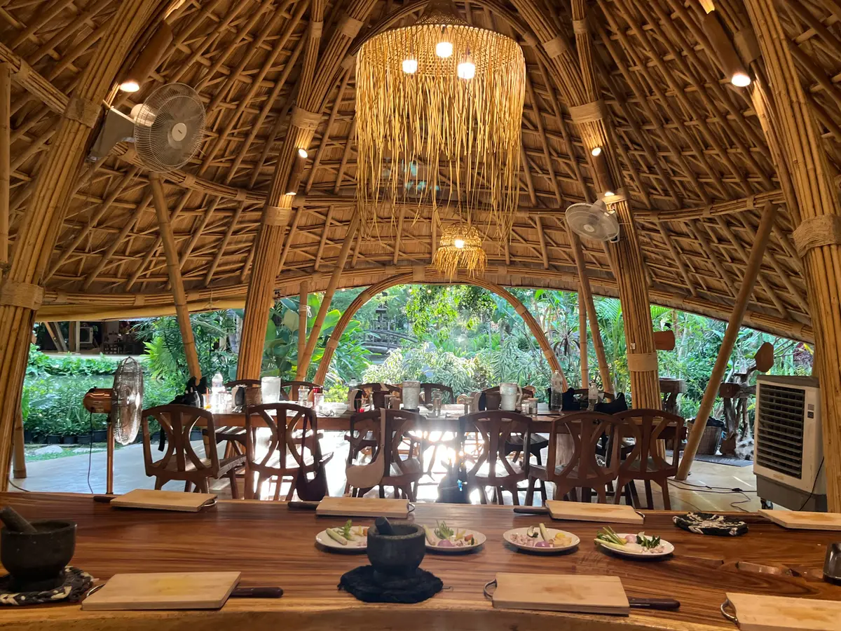 Wooden counters set with plates and mortars under a woven bamboo roof, with tables beyond.
