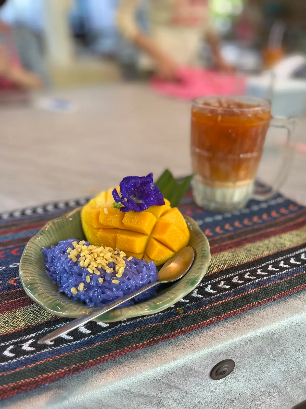 Mango with purple sticky rice on a plate, with an iced Thai tea behind.