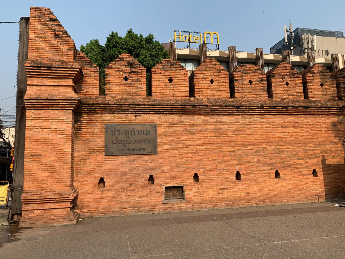 Red brick city wall with a stone plaque at street level in the old moat area.