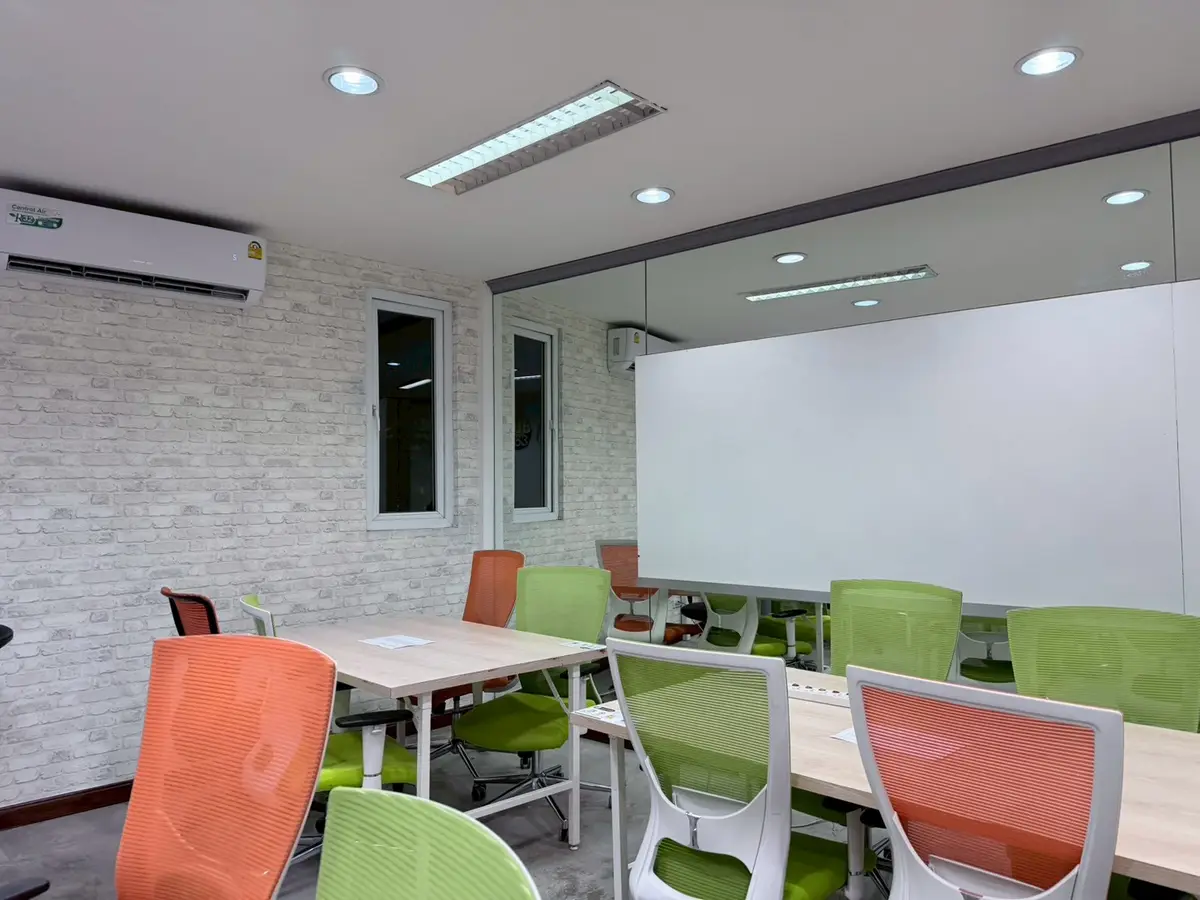 Meeting room with a whiteboard, white tables and green and orange chairs.