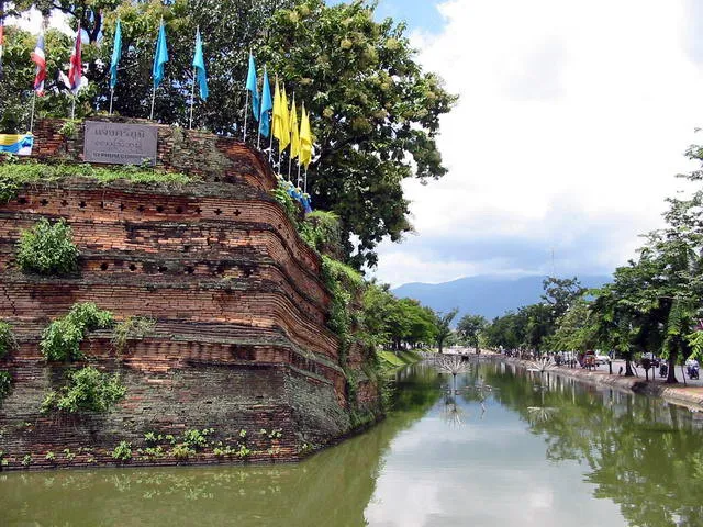 Water in the city moat beside a sloping brick bastion with flags and trees