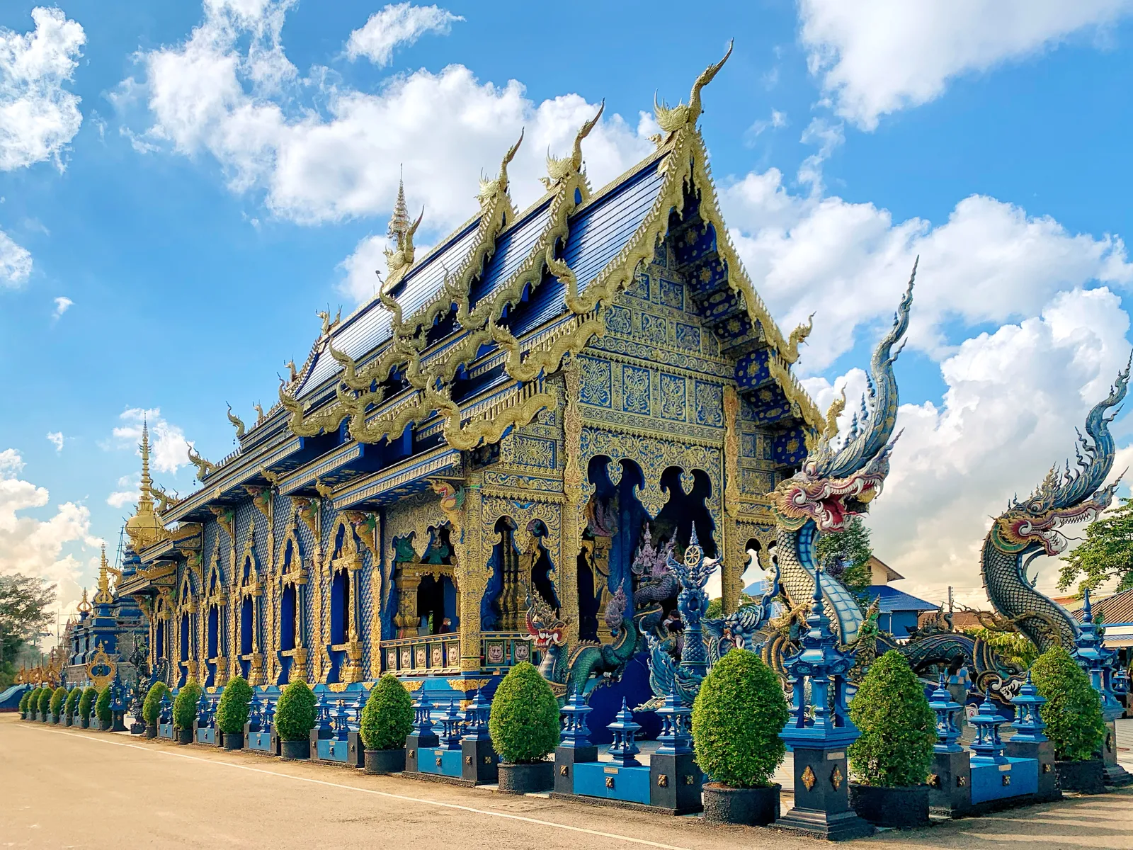 Blue and gold temple hall with dragon statues beside it under a cloudy sky
