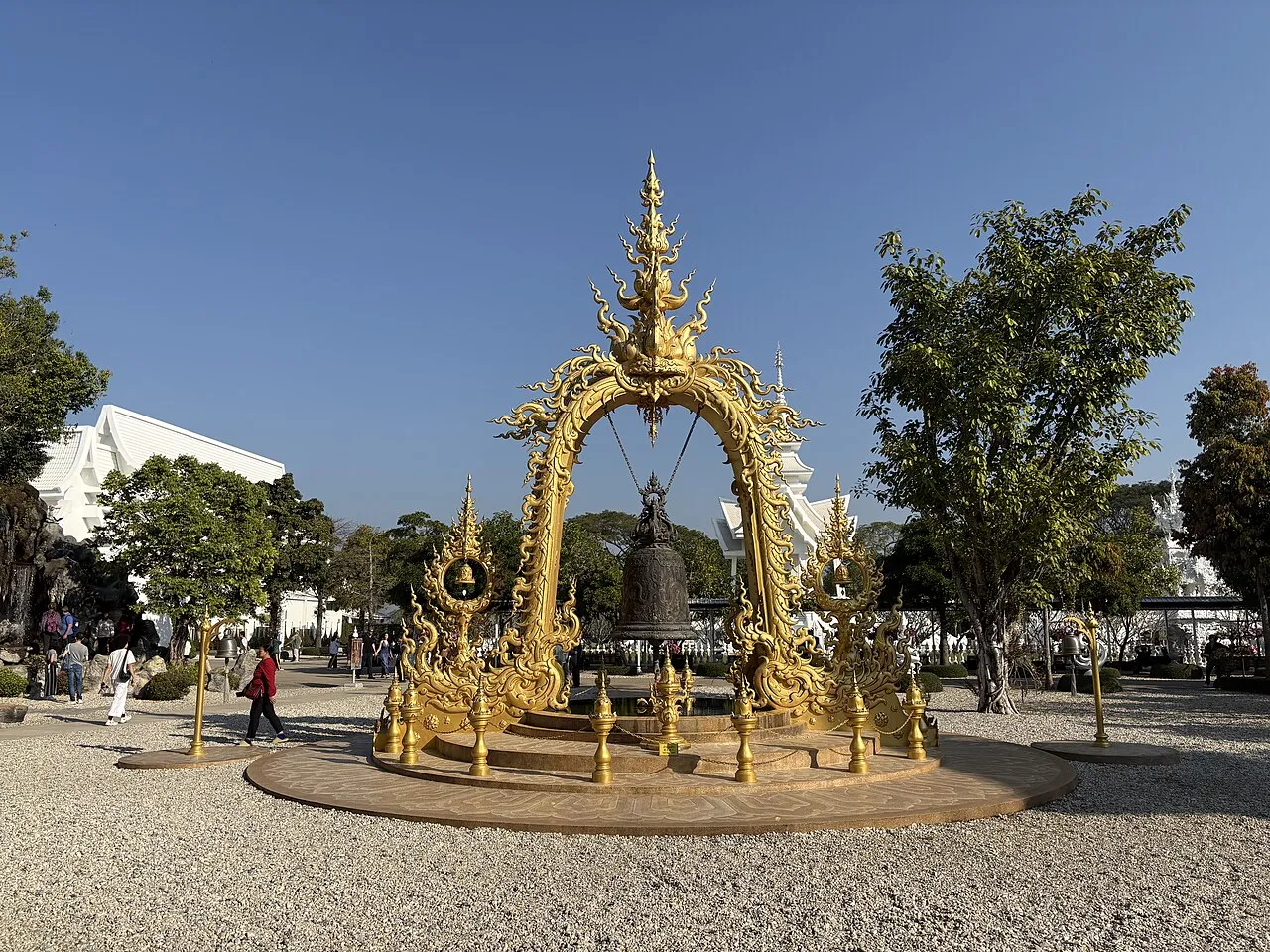 Golden bell under an ornate gold arch on a gravel courtyard