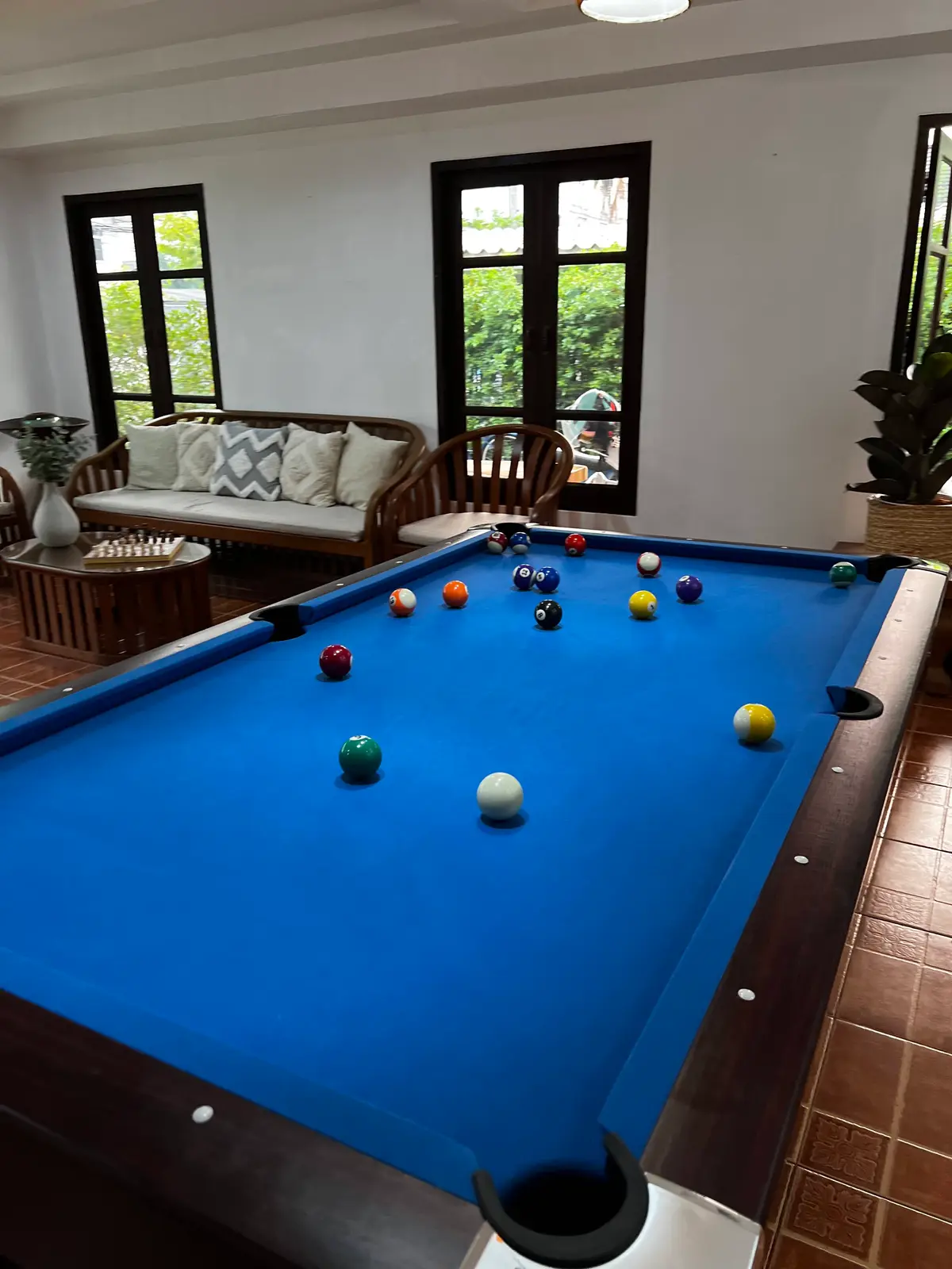 Blue pool table in a room with a wicker sofa and a tiled floor.
