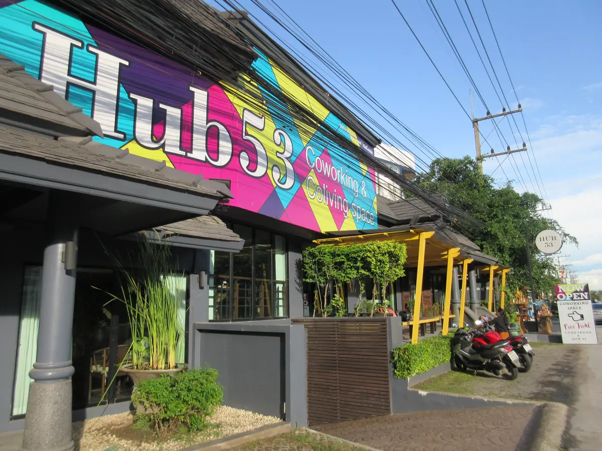 Colourful painted sign above the entrance of a low building with parked motorbikes and plants.