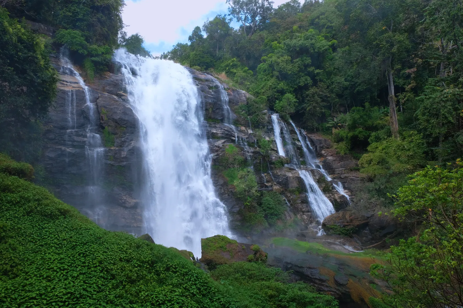 Tall white waterfall dropping down a rock face into green forest