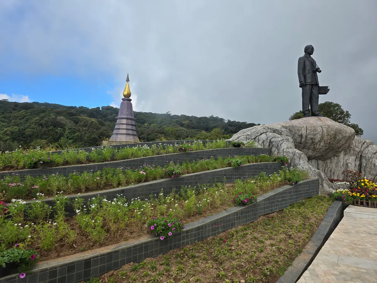 Statue on a rock above stepped flower terraces with a grey pagoda in the distance