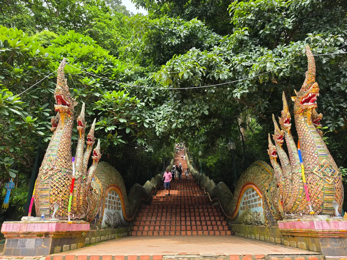 Two multi-headed naga serpent statues flanking a brick staircase that climbs through trees