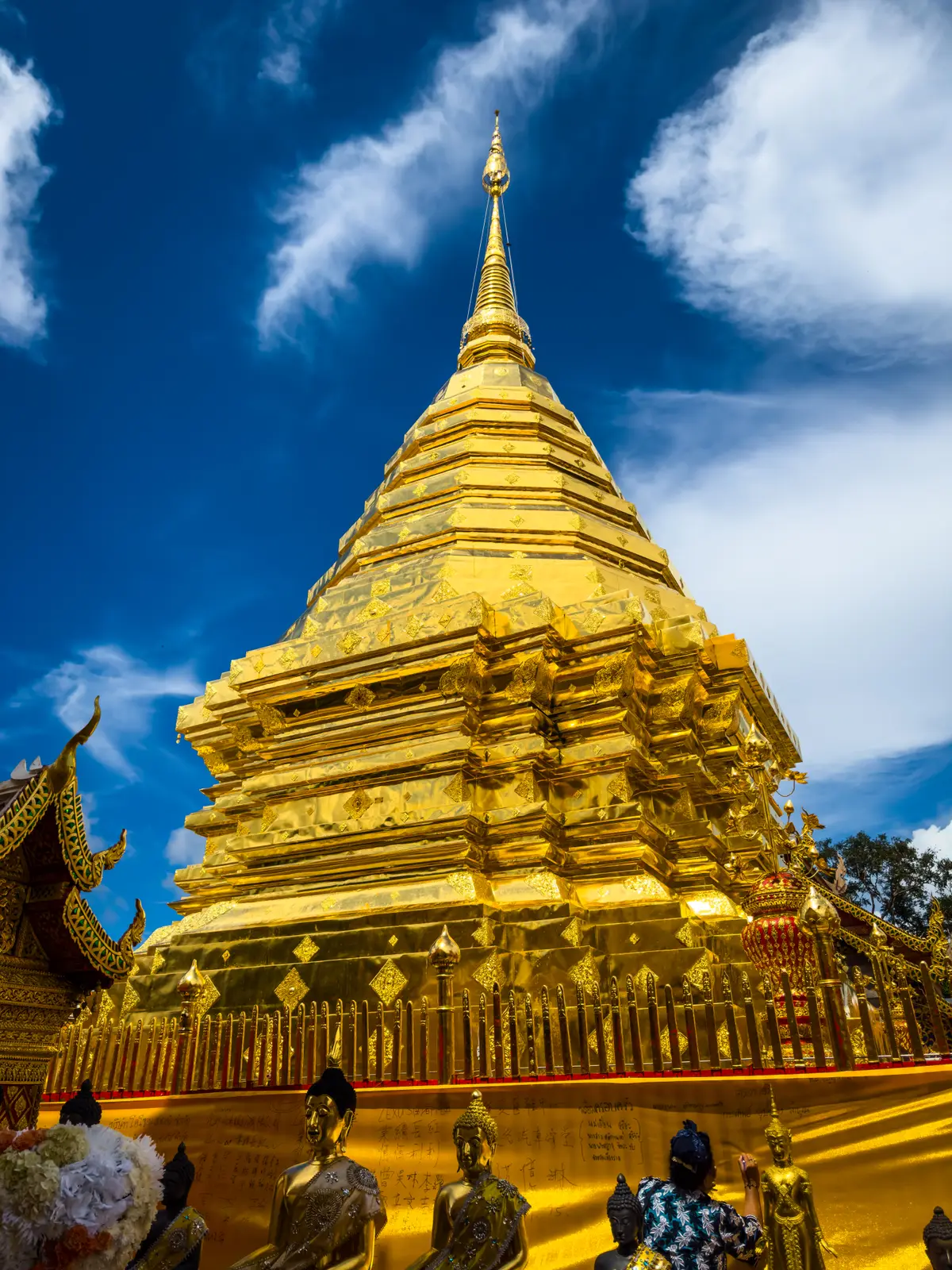 Gold-plated chedi against a blue sky with a corner of a roof in the foreground