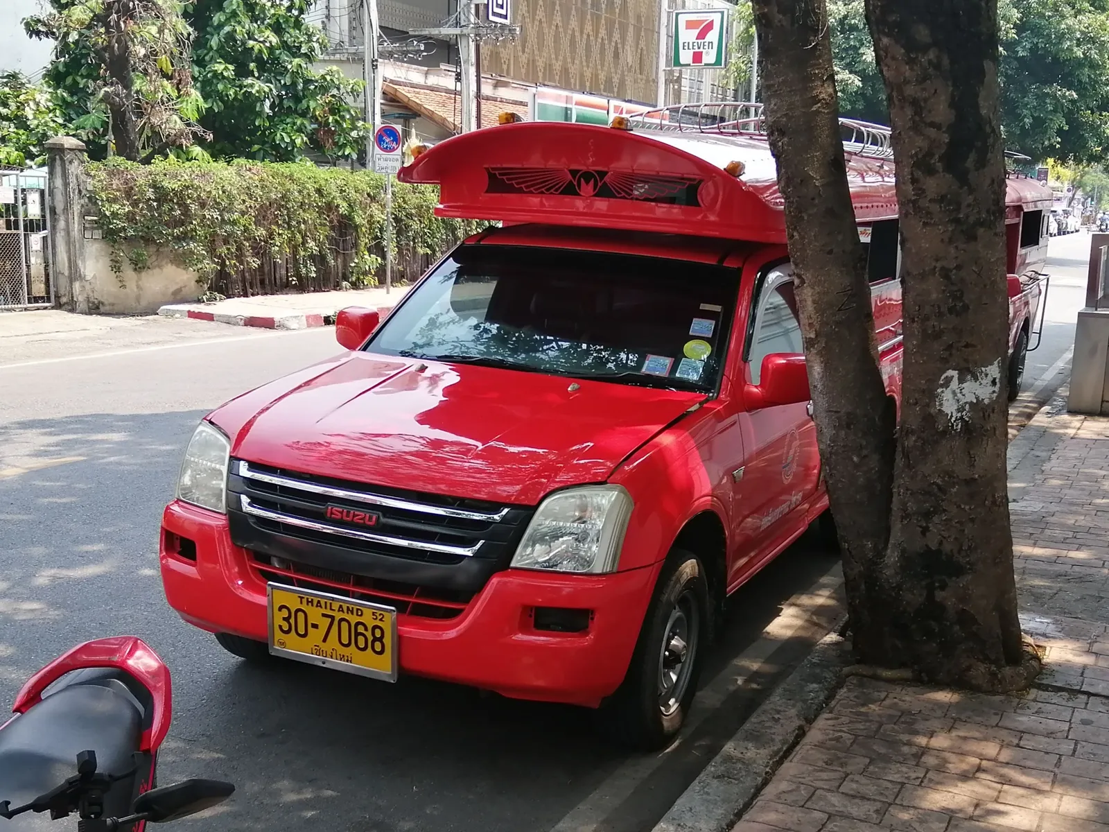 Red pickup truck with a raised rear canopy parked at the kerb beside a tree