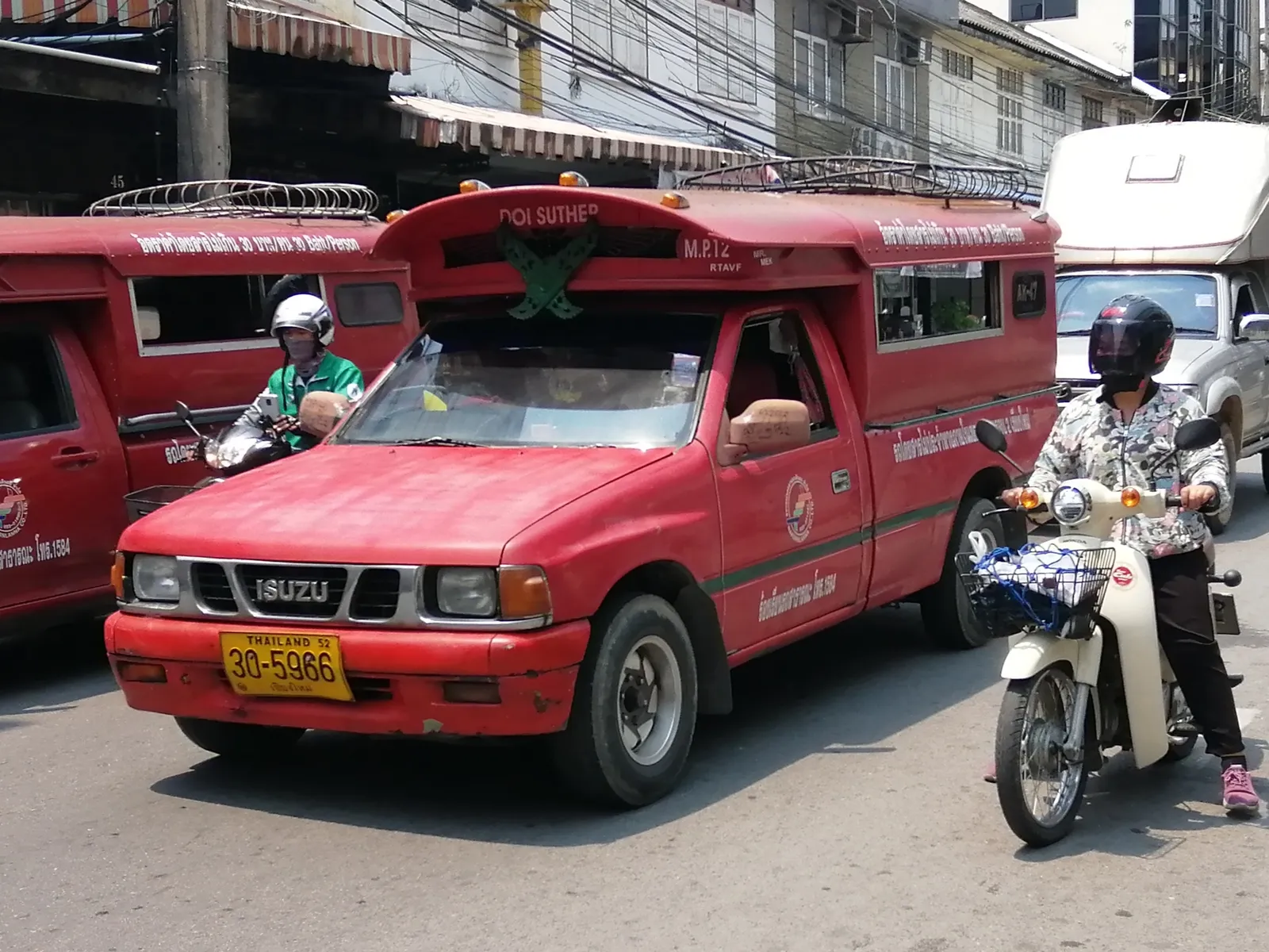Red pickup truck with a covered bed on a street with a motorbike beside it