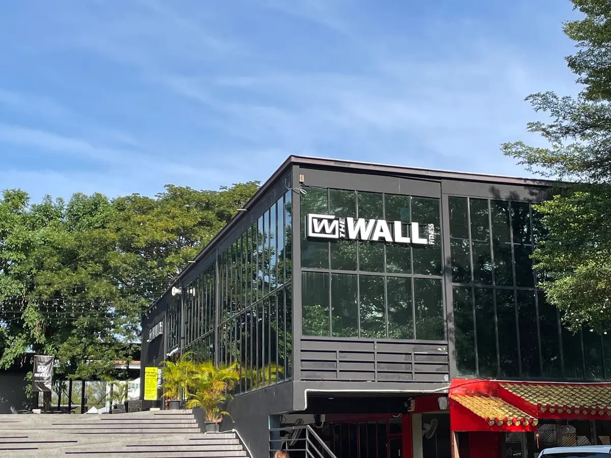 Dark glass-fronted gym building with a Wall logo above the entrance steps.