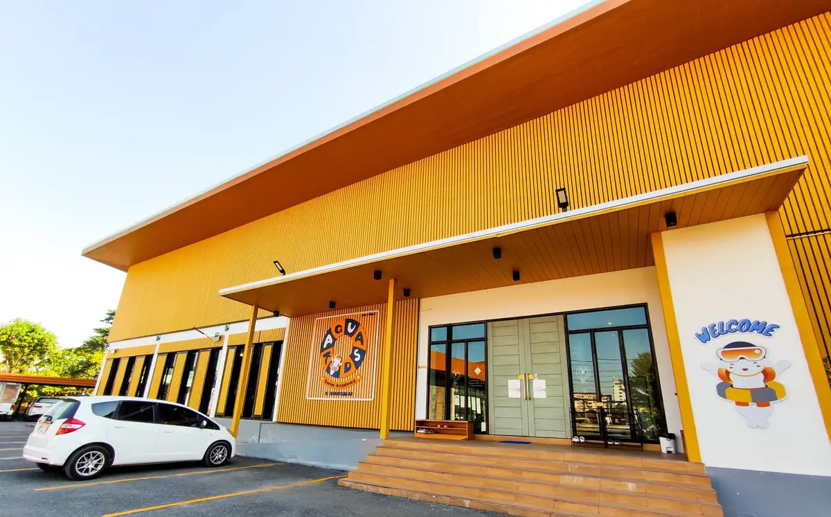 A yellow slatted-wood building with a wide entrance and a car parked at the front.