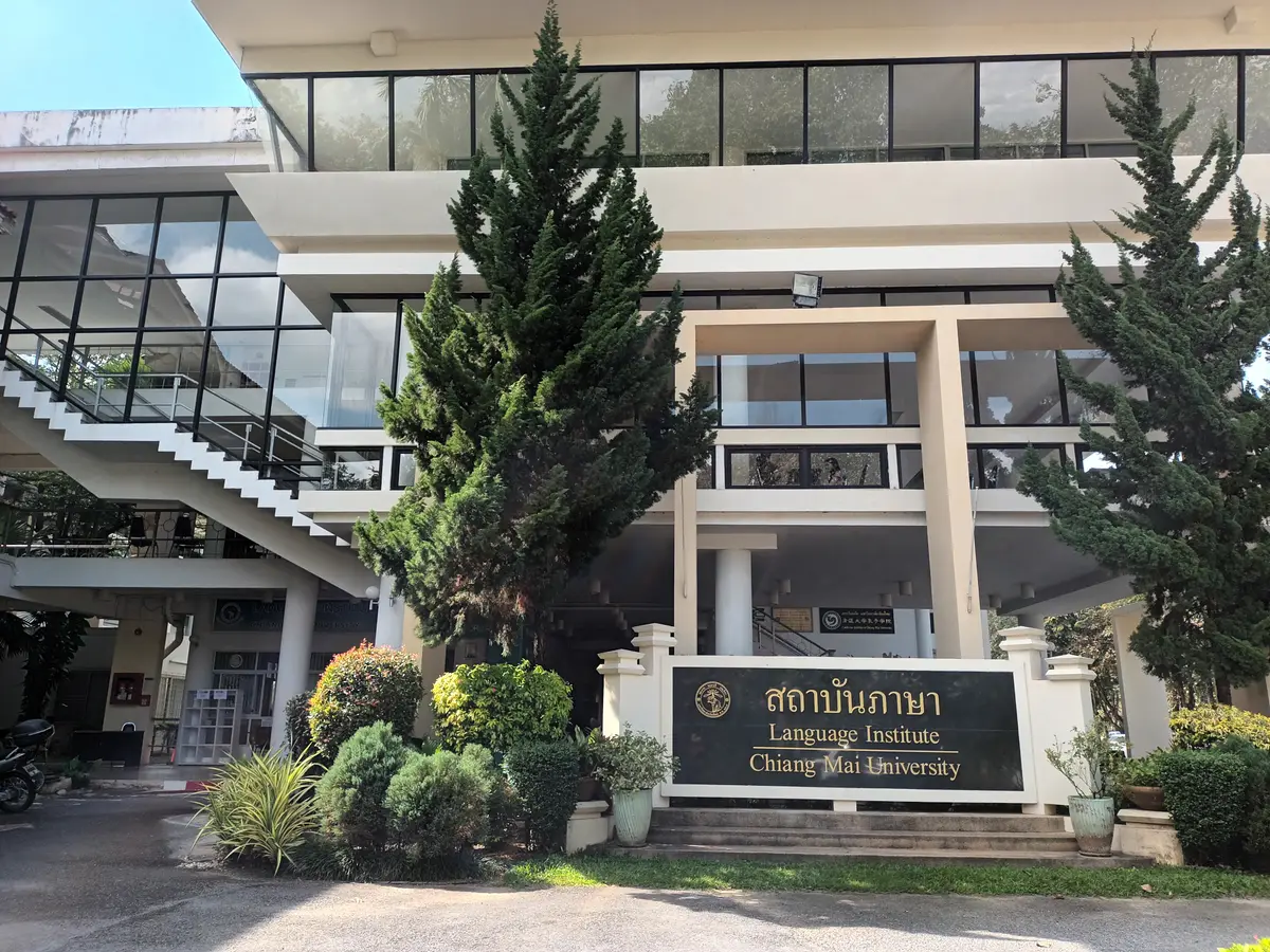 Concrete university building behind pine trees and a signboard reading Language Institute, Chiang Mai University