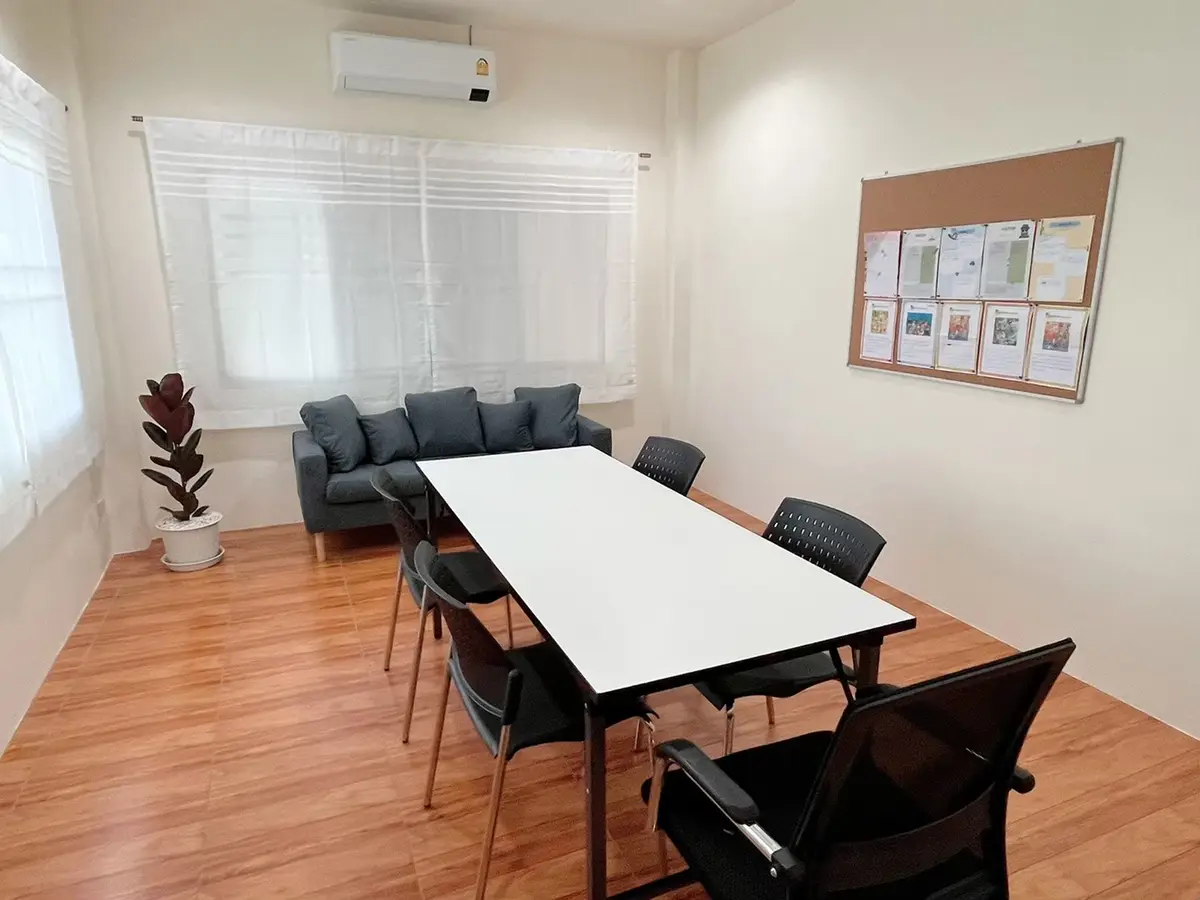 Small meeting room with a long white table, black chairs, a grey sofa and a notice board