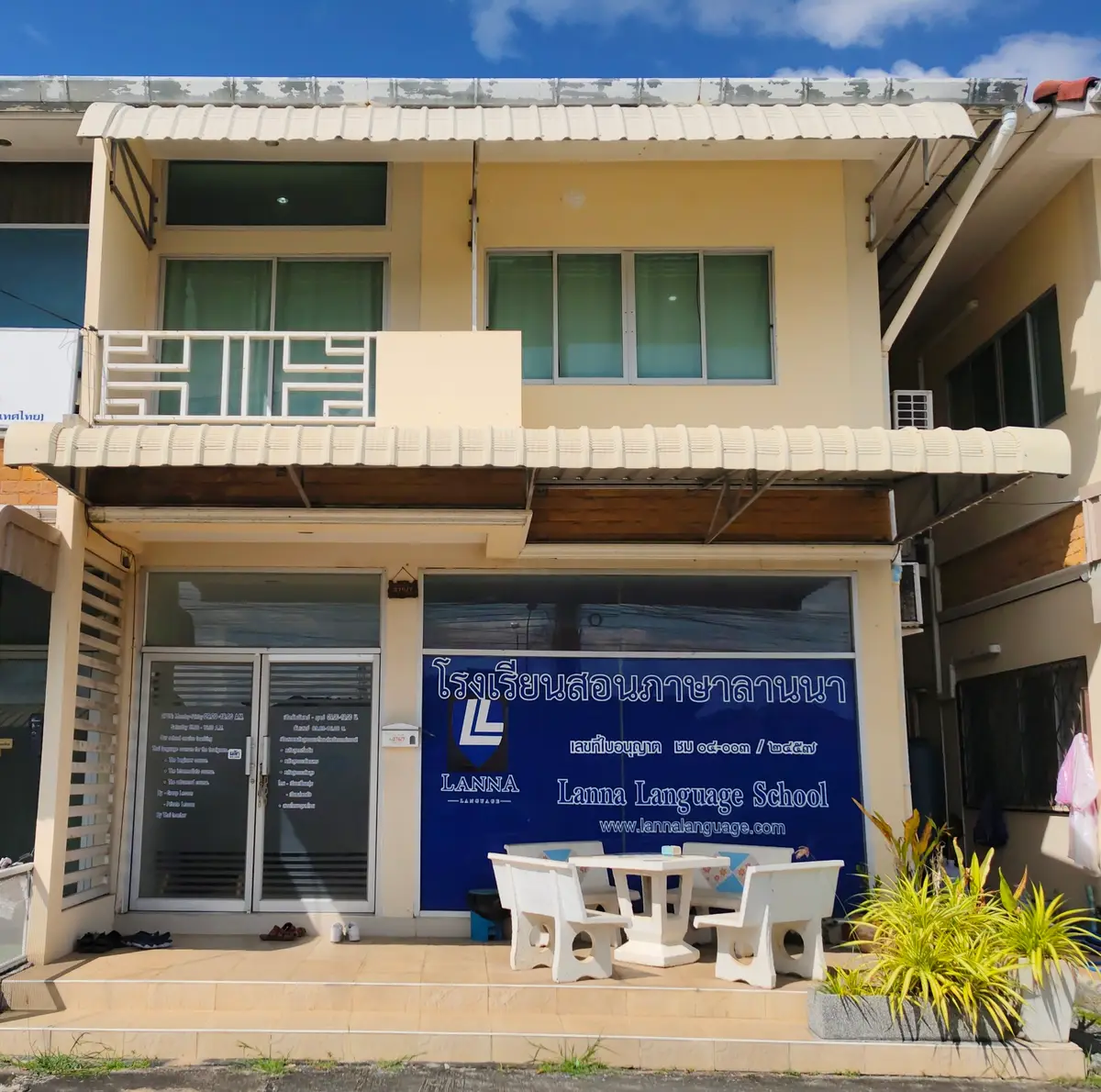 Two-storey townhouse with a blue Lanna Language School sign and white garden chairs outside