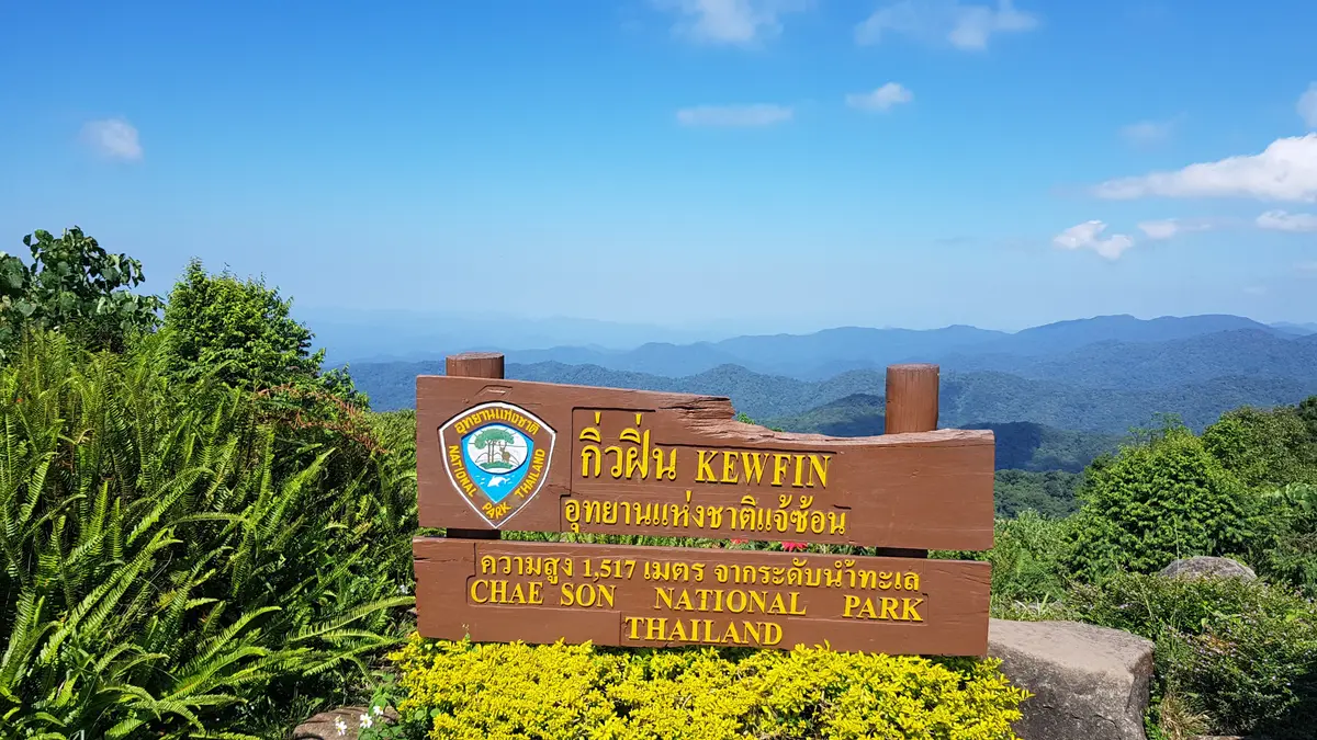 Brown wooden national park sign with Thai and English lettering in front of blue distant mountains