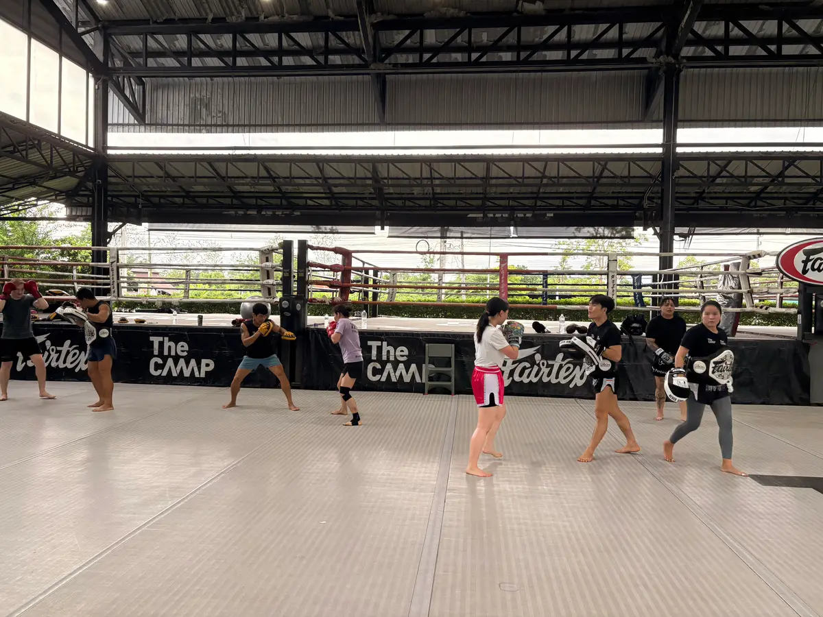 Group in a large open-sided hall practising pad work in pairs.