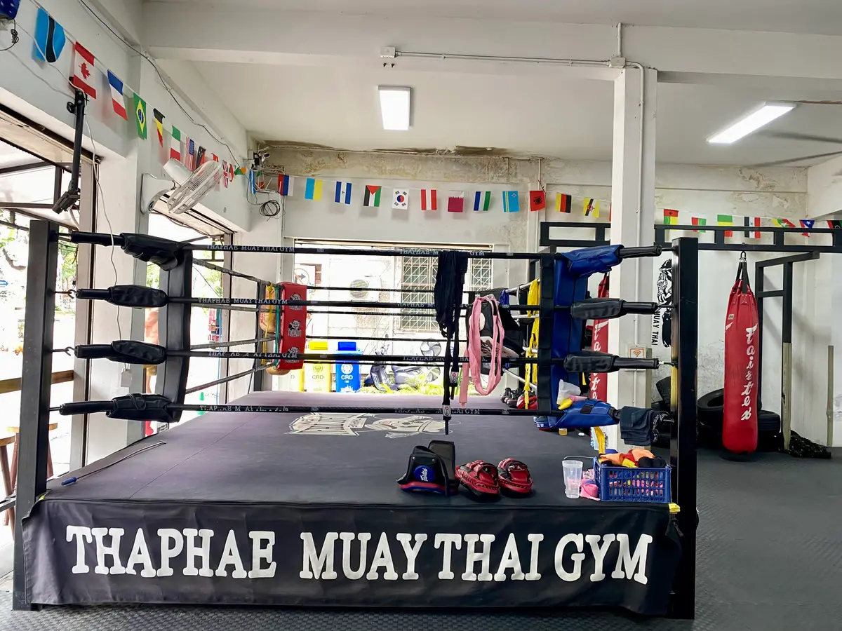 Boxing ring with a banner on the apron reading the gym name and string flags on the wall.