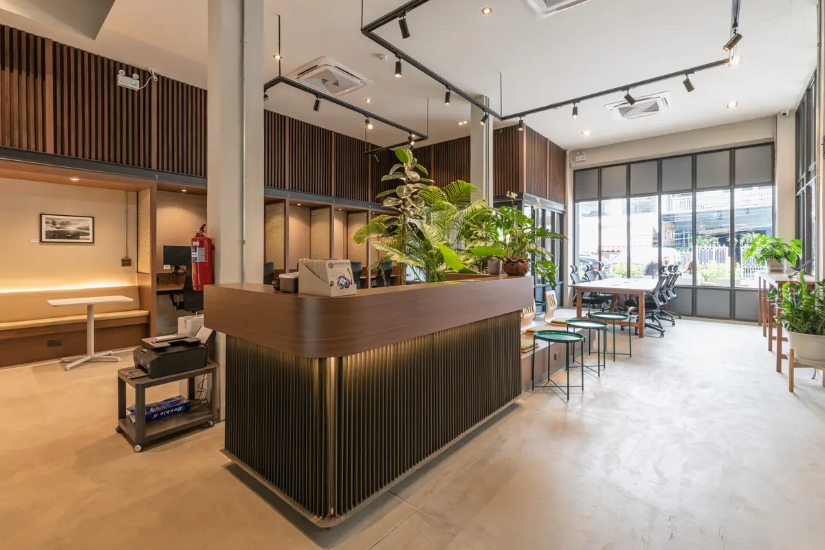Reception desk with a wooden front and shelves of plants in a bright co-working space