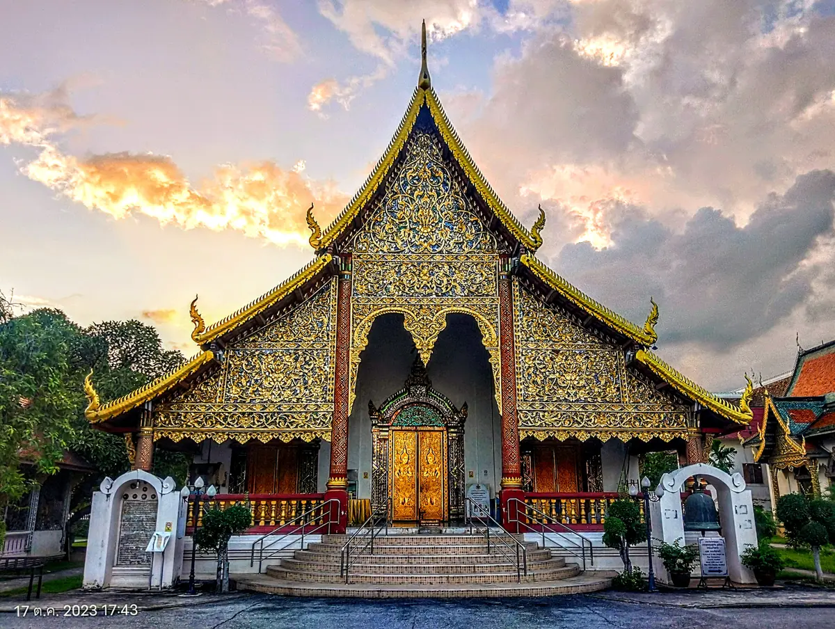 Gold-decorated temple hall front with a tiered roof and a wooden door at sunset