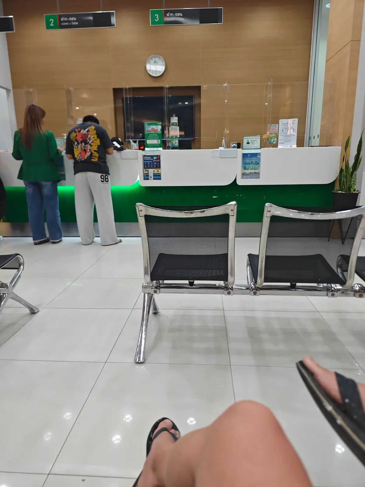 Teller counter with green panels and a row of metal waiting chairs in front of it.
