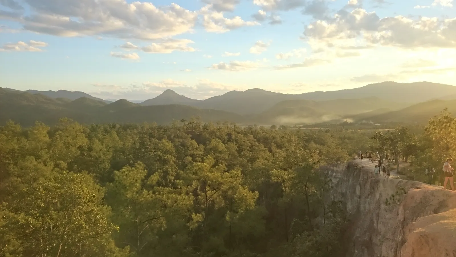 Sunset over forested hills beside a pale cliff edge