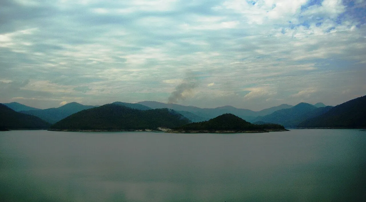Wide reservoir with forested hills and a thin plume of smoke in the distance
