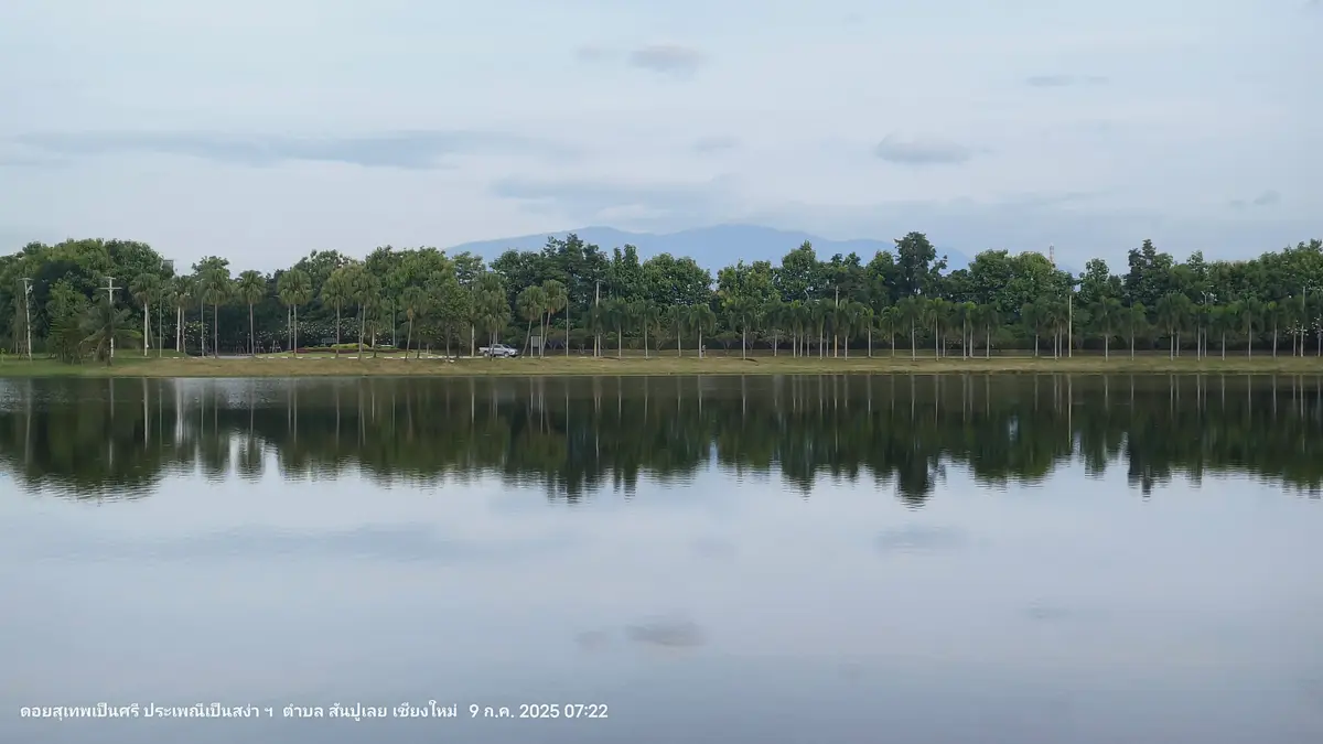 Still lake with a line of trees on the far bank and hills behind