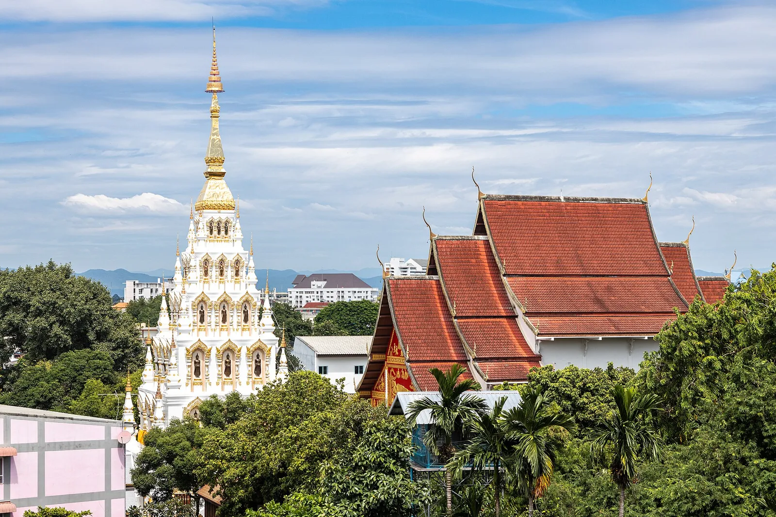 White pagoda and red-roofed temple buildings among trees under a blue sky