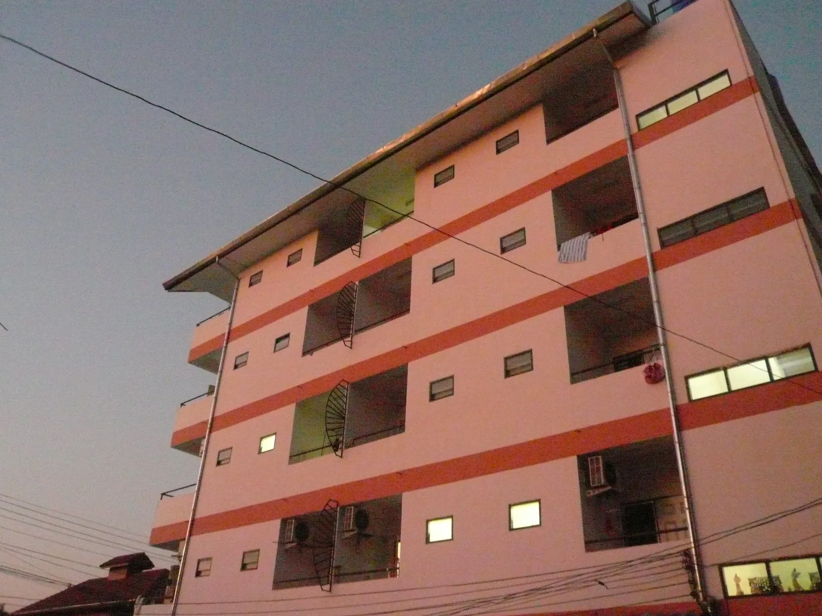 Six-storey pink apartment block with orange bands and lit windows at dusk