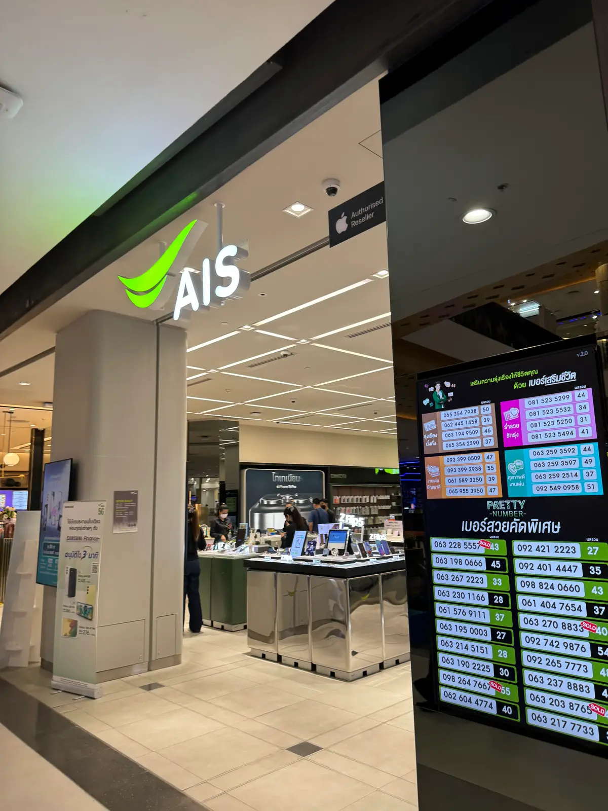 Front of the AIS shop inside a shopping mall, with the green AIS logo above the counter and a queue number screen on the right.