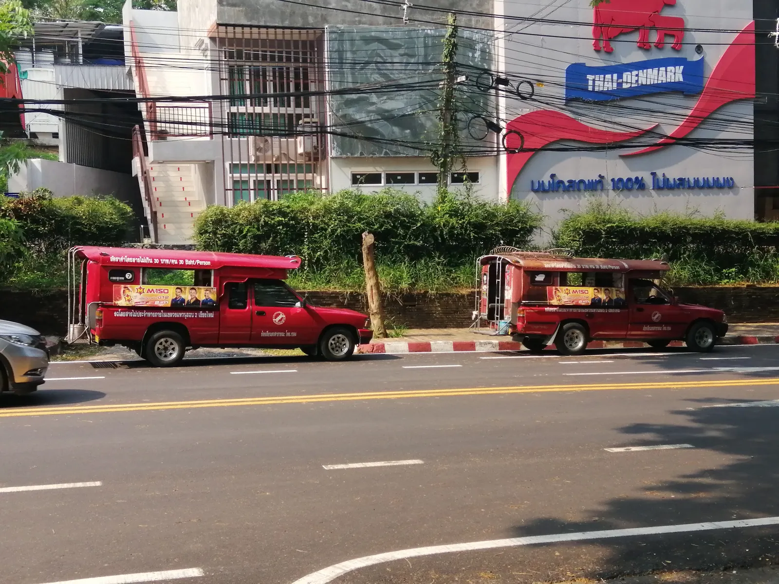 Two red pickup trucks parked in line at the roadside outside a shop front