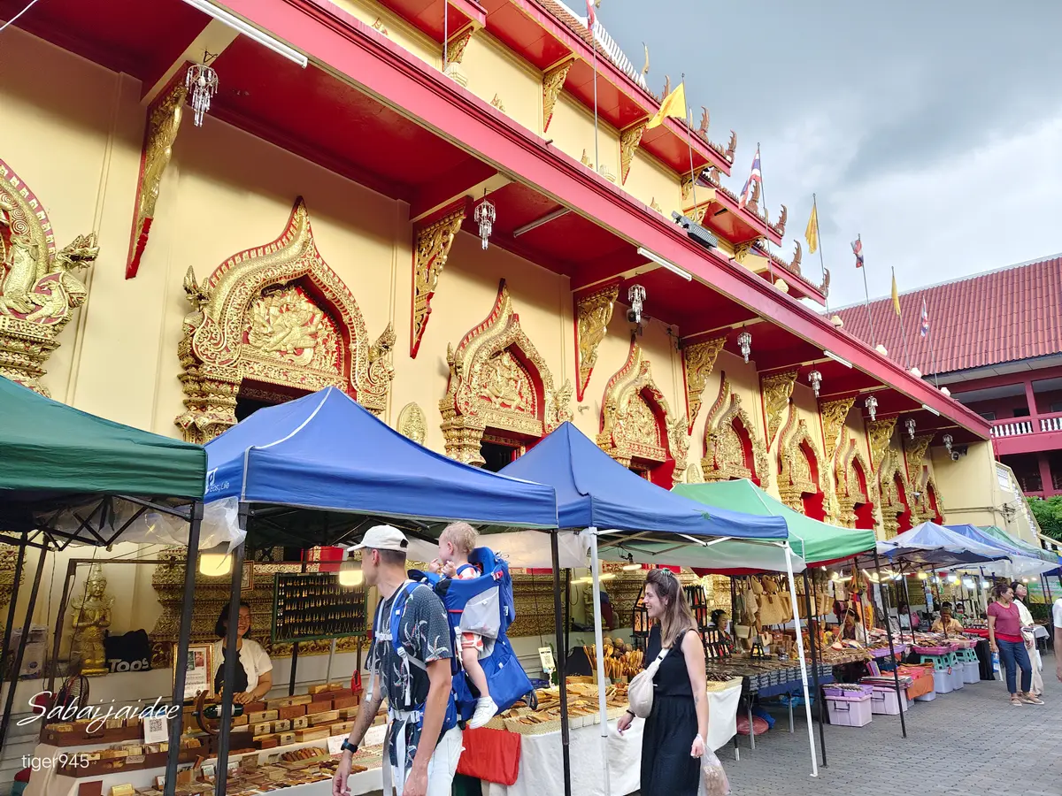 Blue and green stall canopies in front of a temple building with a gold and red gabled roof.